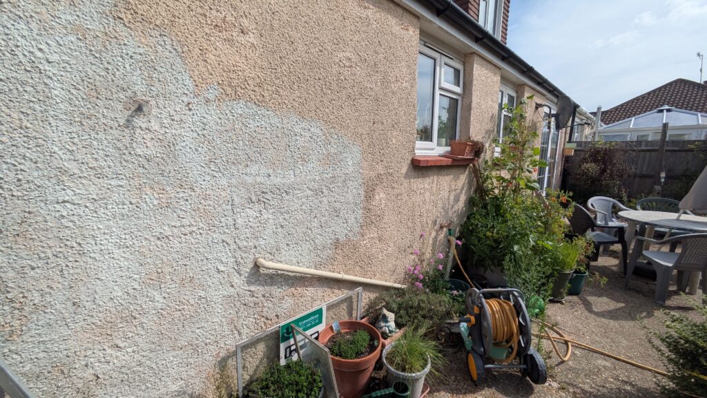 Stained and ageing exterior masonry paint on a bungalow in Tarring