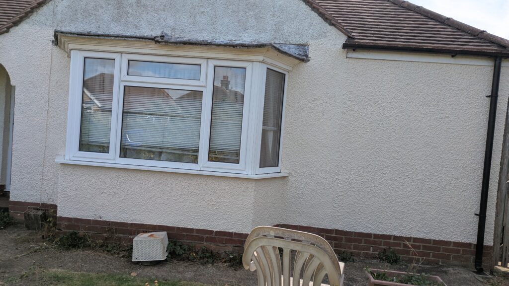 Stained and ageing exterior masonry paint on a bungalow in Tarring